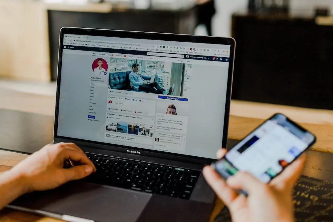Person using a laptop and phone to manage a Facebook page